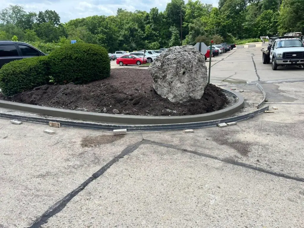 Completed commercial concrete curb and landscape island with boulder in a parking lot