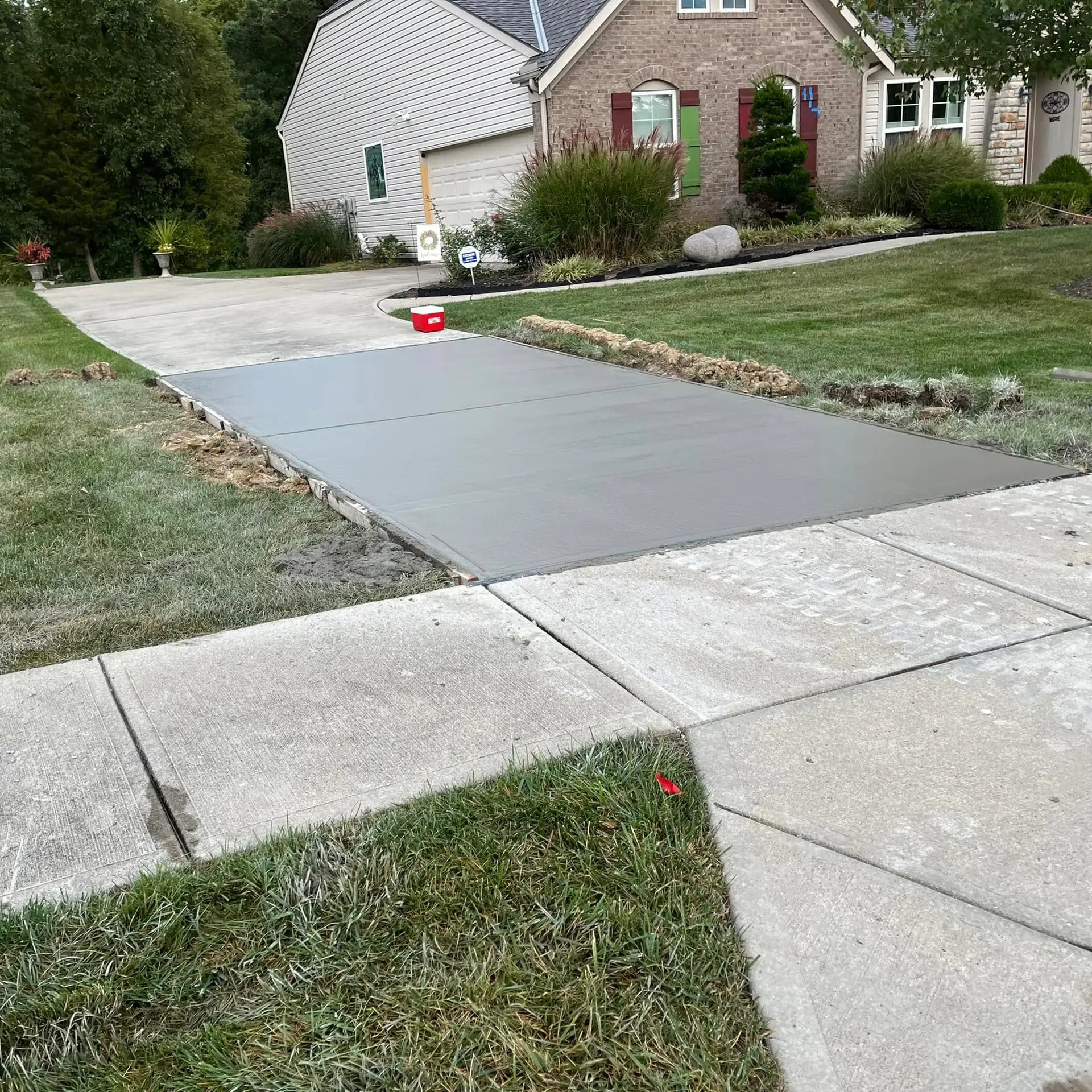 Fresh concrete driveway extension with broom finish poured next to an existing residential driveway