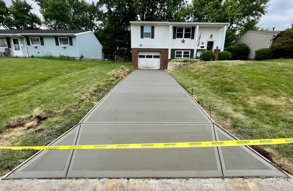 Newly poured concrete driveway with broom finish leading to split-level home, caution tape across fresh pour