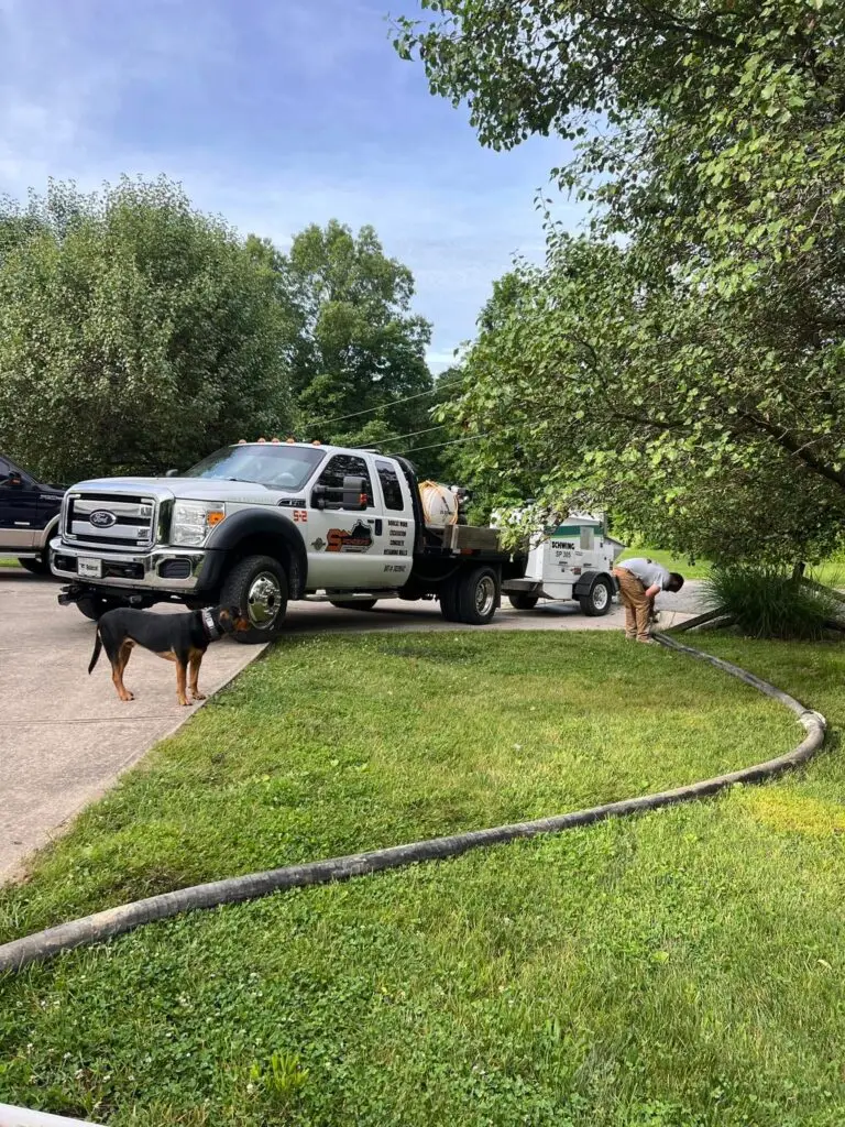 Spencer's Ford line pump truck running concrete hose across residential lawn with dog watching