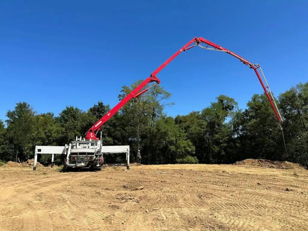 Red concrete line pump truck with boom extended over residential foundation pad in Northern Kentucky