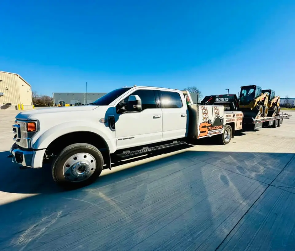 Spencer's Outdoor Solutions branded Ford F-450 service truck hauling Cat skid steer on trailer
