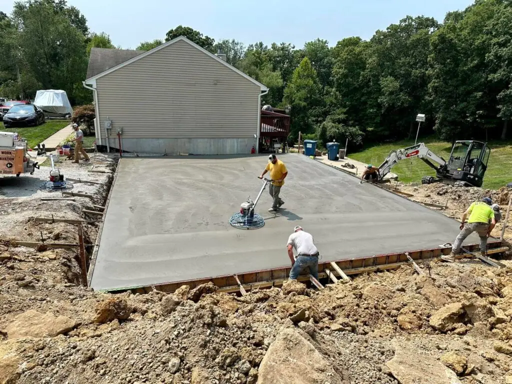 Crew finishing large concrete slab pour with power trowel and bull float at residential addition