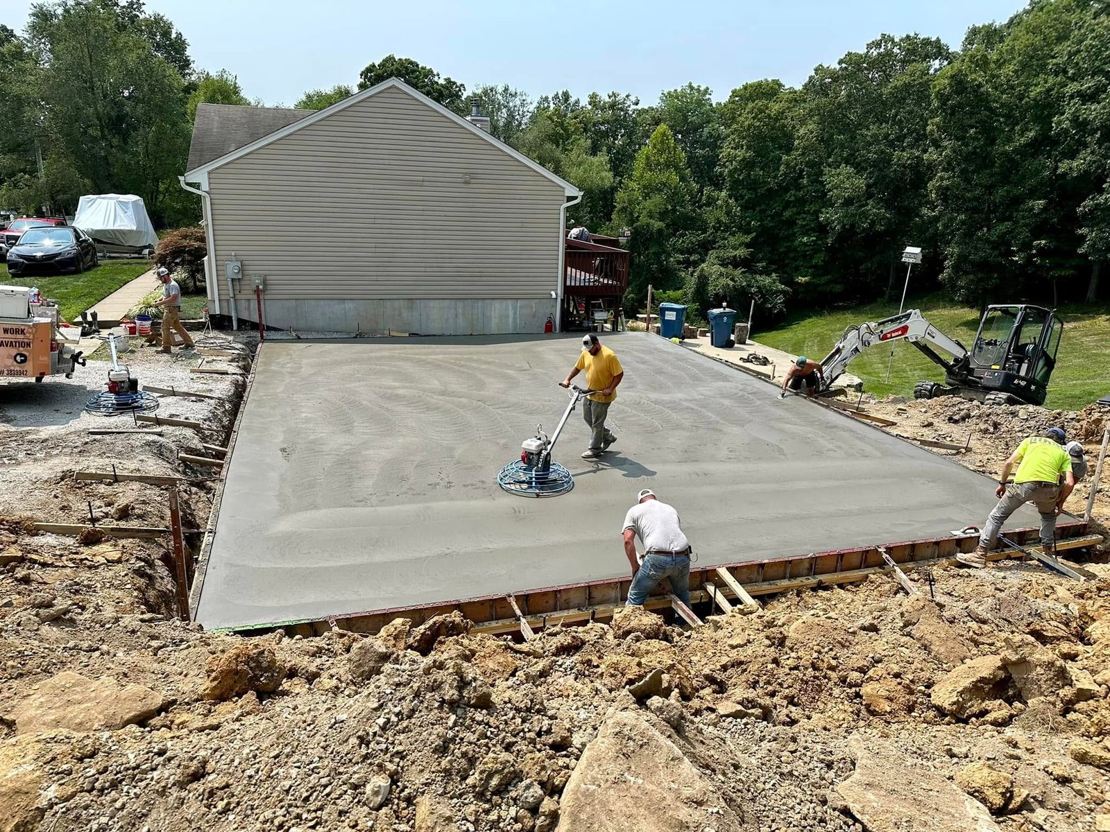 Crew finishing a large concrete slab with bull float and power trowel