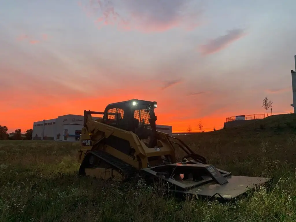 Skid steer bush hogging an overgrown lot at sunset in Northern Kentucky
