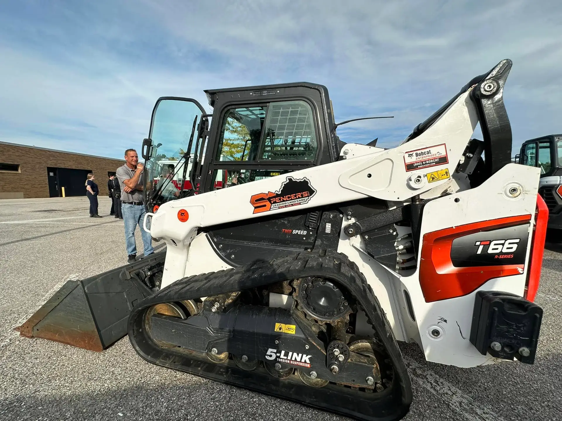 Spencer's Outdoor Solutions branded Bobcat T66 compact track loader at equipment showcase with owner nearby