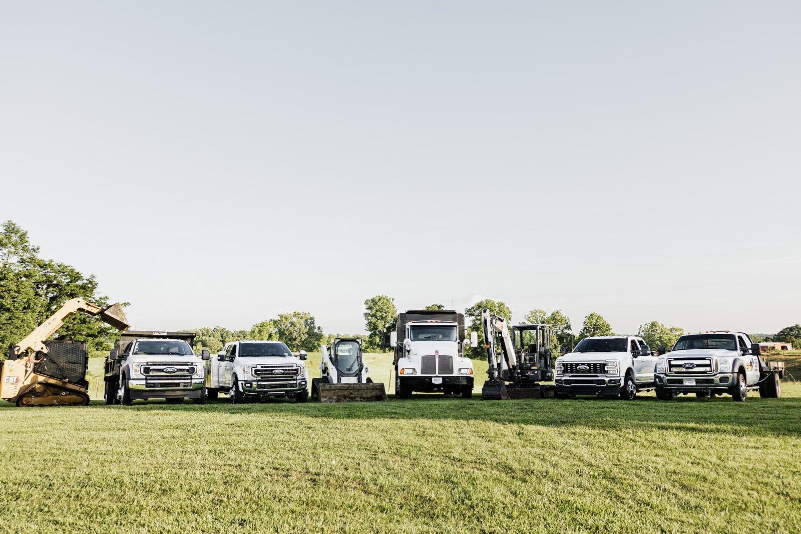 Spencer's Outdoor Solutions equipment fleet lineup with trucks, Bobcat skid steer, pump truck and mini excavators